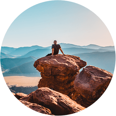 Hypnosepraxis Reyes - Mann sitzt auf Felsen in der Wüste und schaut auf Berge am Horizont