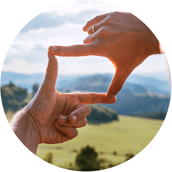 Hypnosepraxis Reyes - Berlin Prenzlauer Berg - fokussiertes Erleben: Finger zweier Hände formen Rahmen vor hügeliger Landschaft